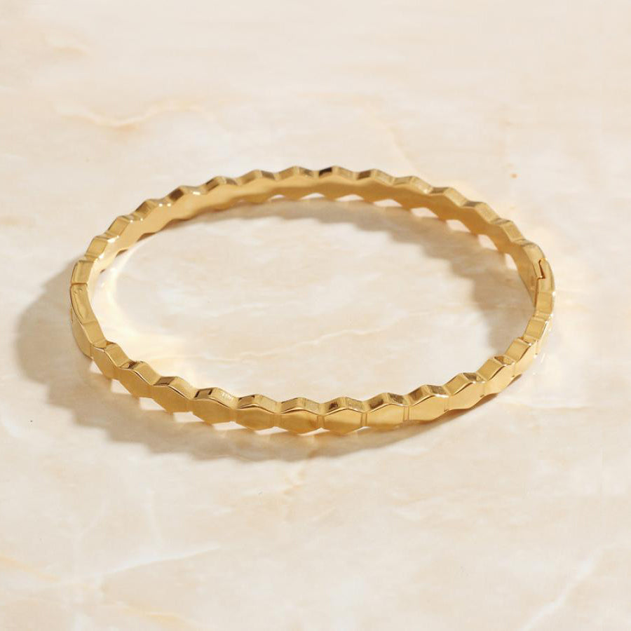 Gold Hexagonal Honeycomb Bangle Bracelet on smooth marble background.