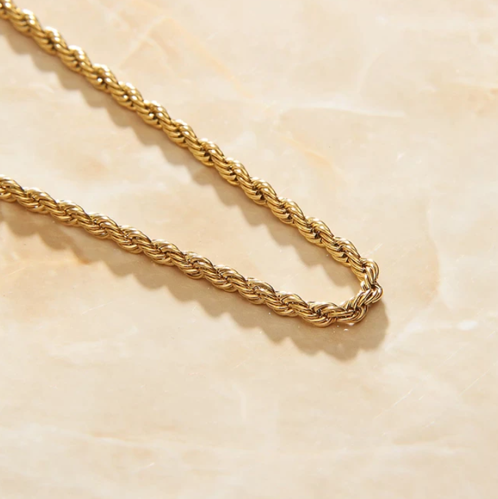 A Gold Rope Chain Necklace laying diagonally on an apricot marbled background.