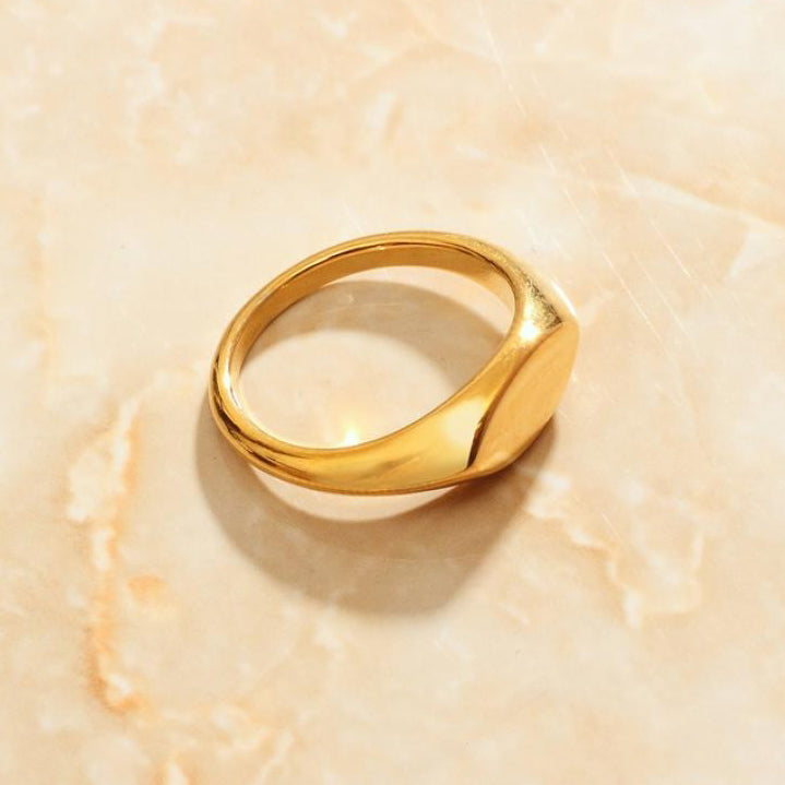 A minimalist Gold Small Oval Signet Ring laying on a marbled surface.