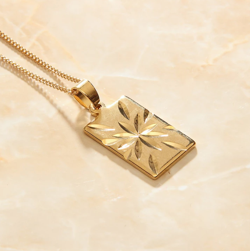 Gold Starburst Pendant on a simple gold chain laying on a marbled background.