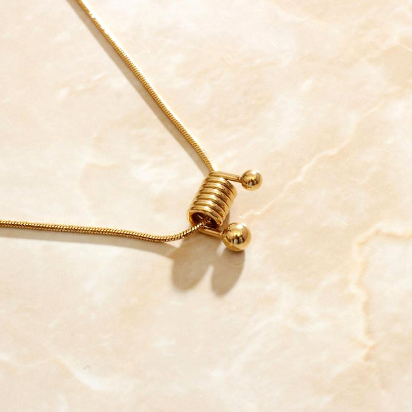 Gold ball spring necklace sitting on a marbled background bathed in sunlight.