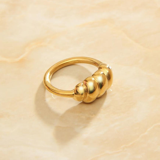 Gold bauble twist signet ring sitting on a marbled background bathed in sunlight.