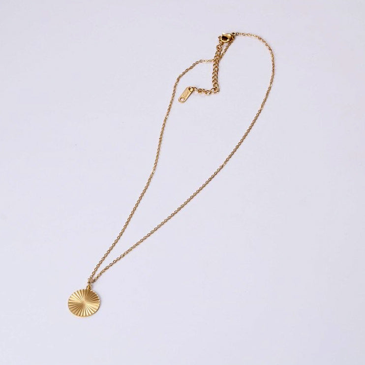 A Gold Circle Sunburst Pendant Necklace sitting on a plain white background.