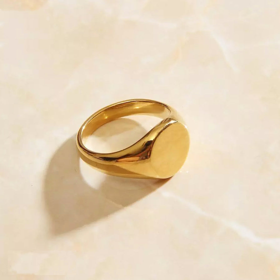 A gold signet ring resting on a sleek marble surface.