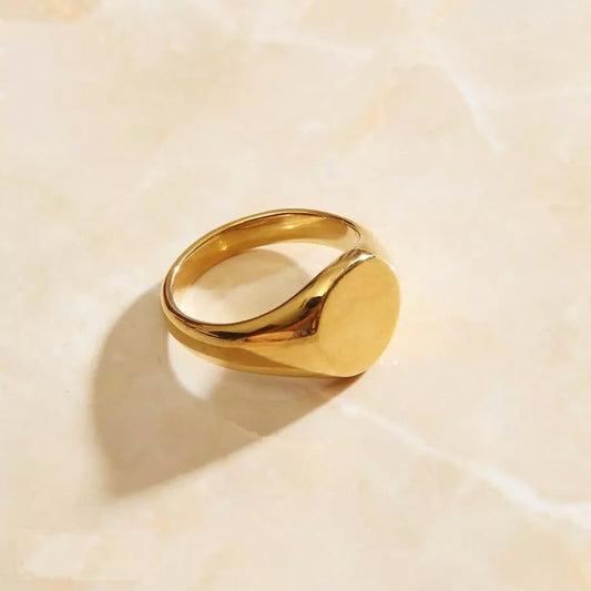 A gold signet ring resting on a sleek marble surface.