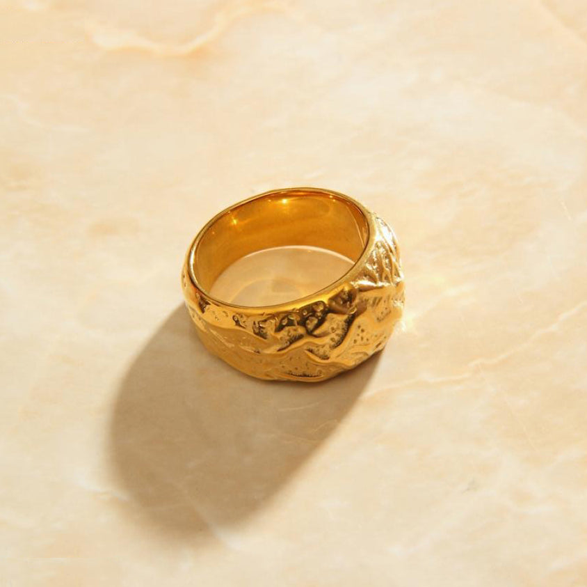 Gold Walnut patterned Signet Ring sitting on a surface of smooth pink quartz.