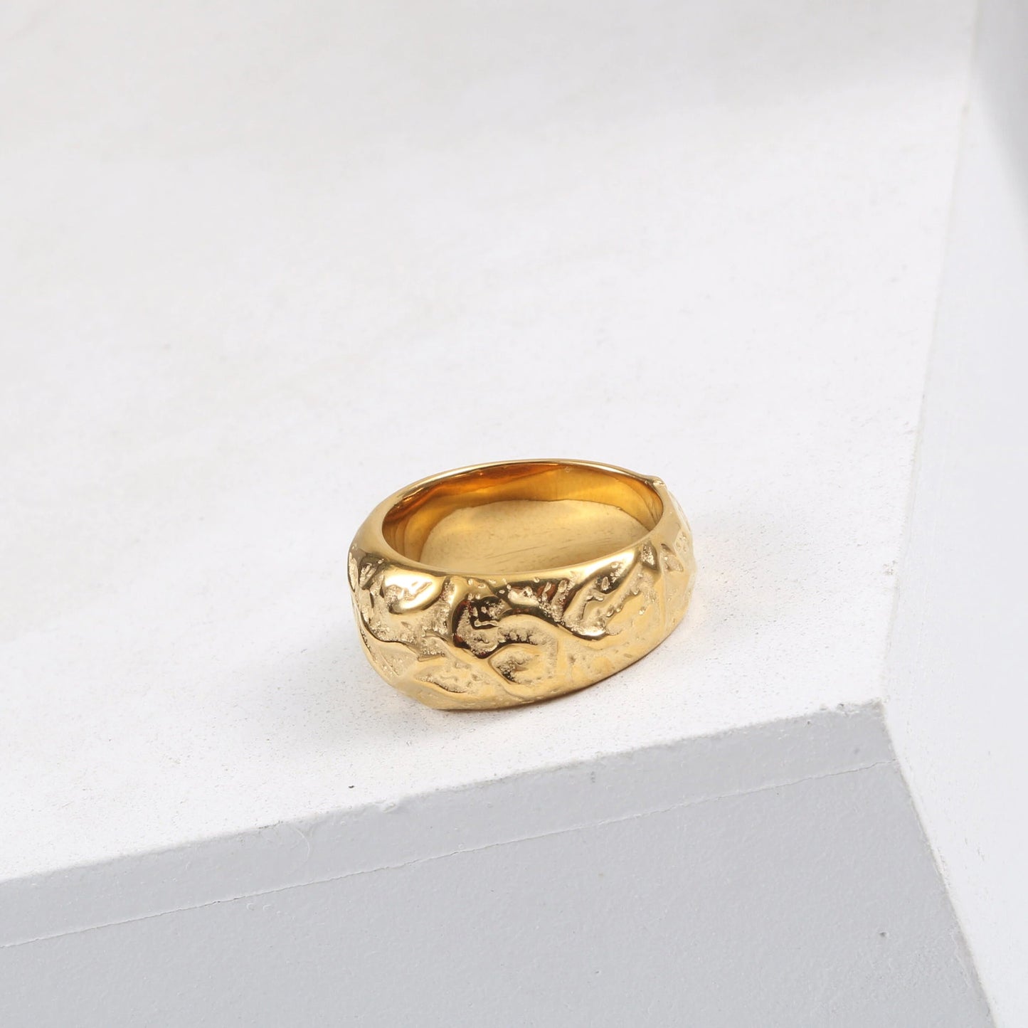 A Gold Walnut Signet Ring shining brightly on a white ledge.