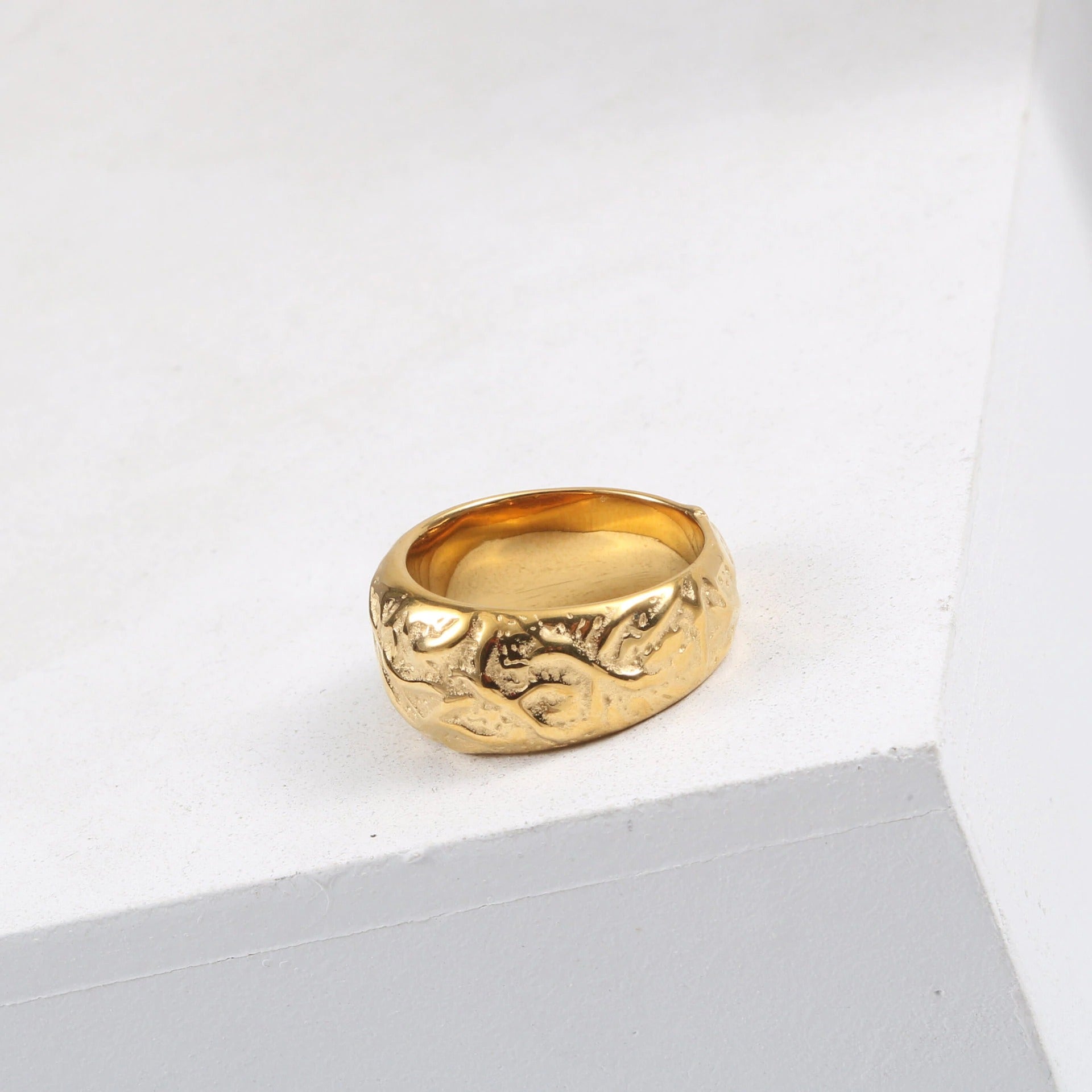 A Gold Walnut Signet Ring shining brightly on a white ledge.