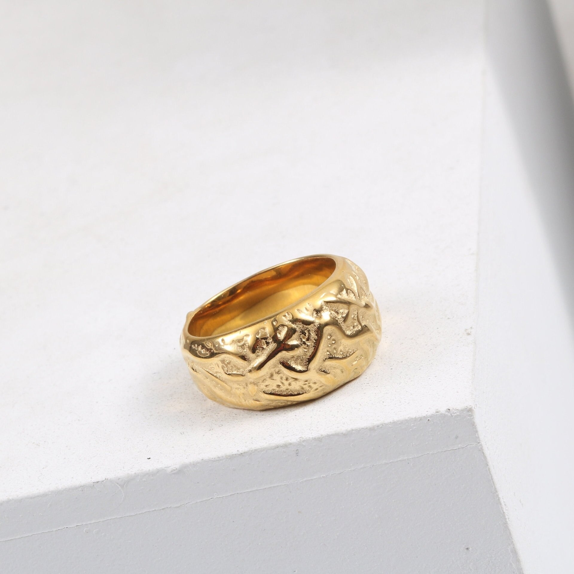 A Gold Walnut Signet Ring shining brightly on a white ledge.
