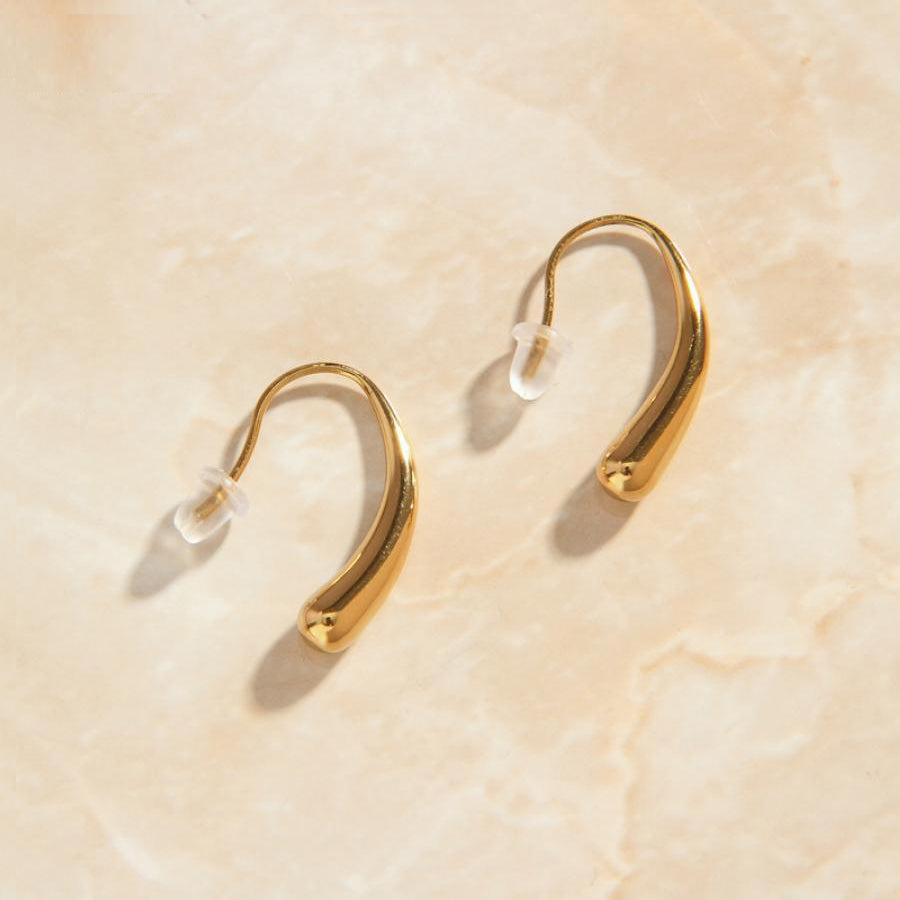 Gold Curved Droplet Earrings on a smooth marble surface in warm sunlight.
