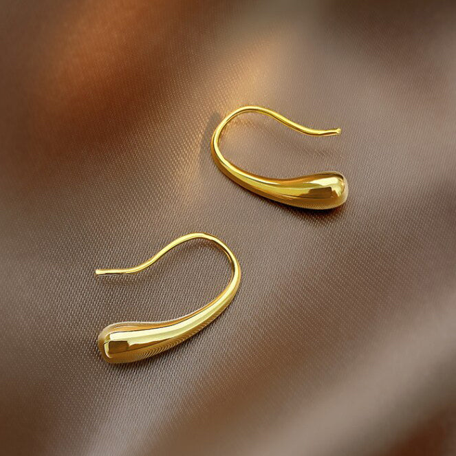 Gold Curved Droplet Earrings shining brightly on a dark textile surface.