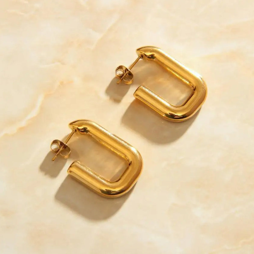 Gold Cut Link Earrings on a smooth quartz background shining in warm sunlight.