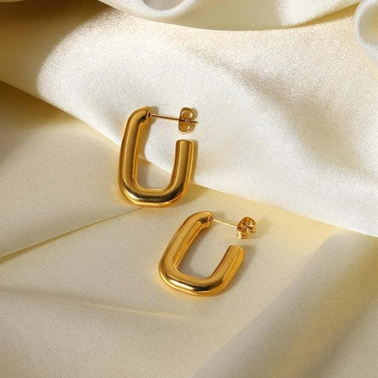Gold Cut Link Earrings laying on a light coloured textile surface.