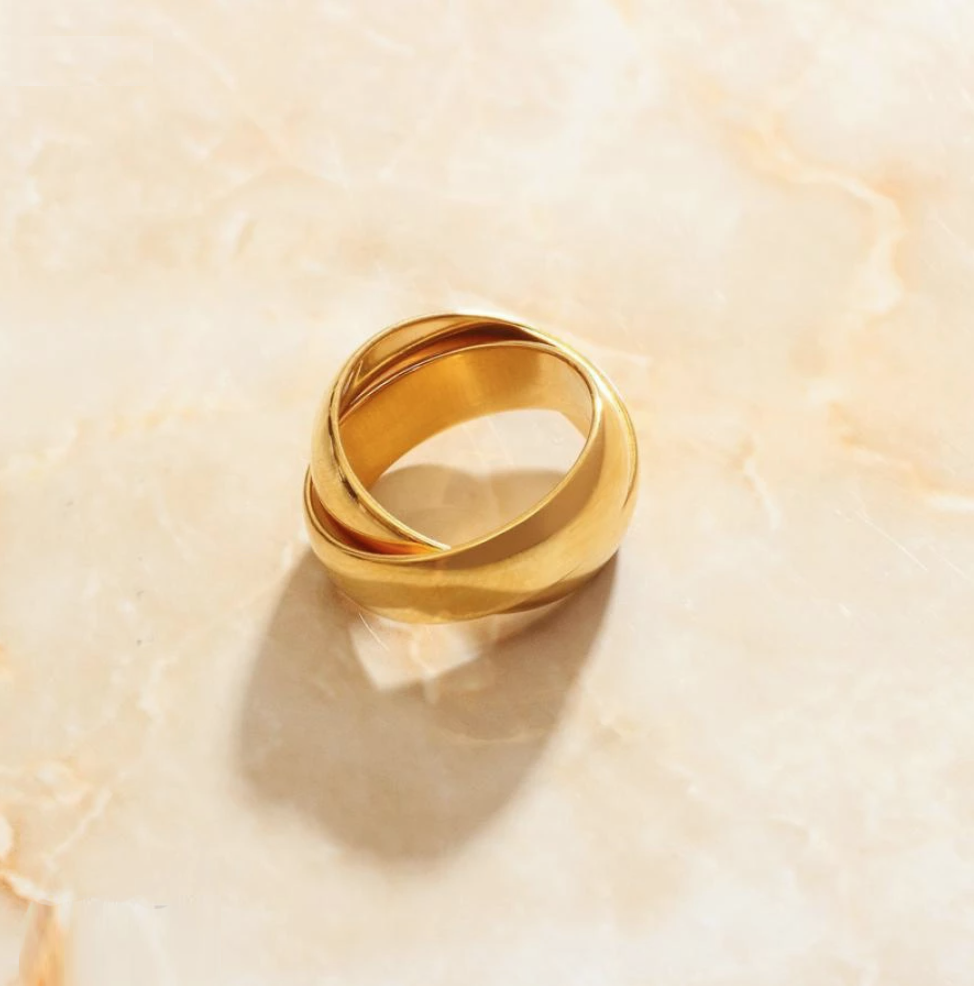 A shiny interlinked gold ring resting on a smooth marble surface.