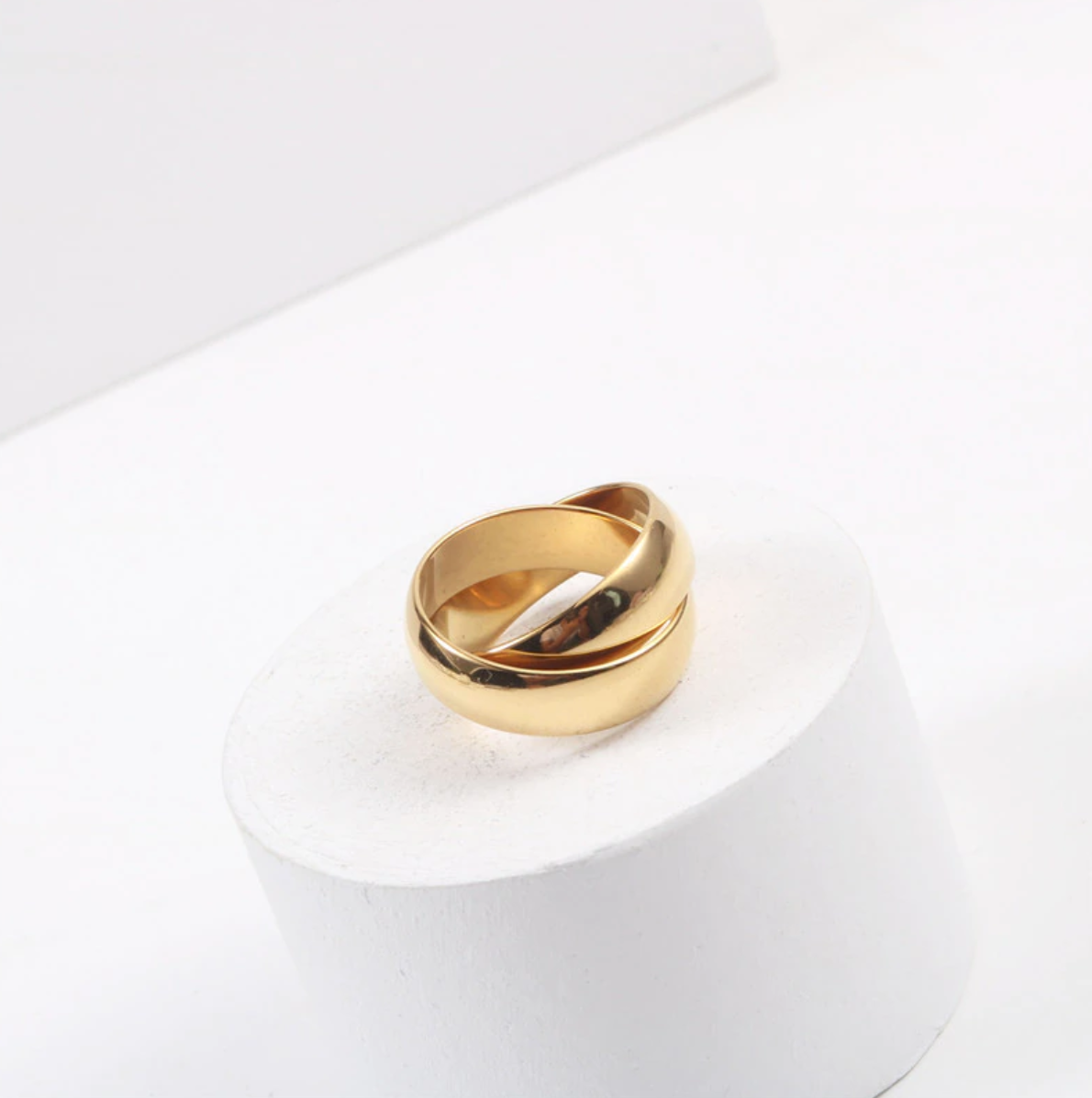 A shiny gold ring resting on a white plinth.