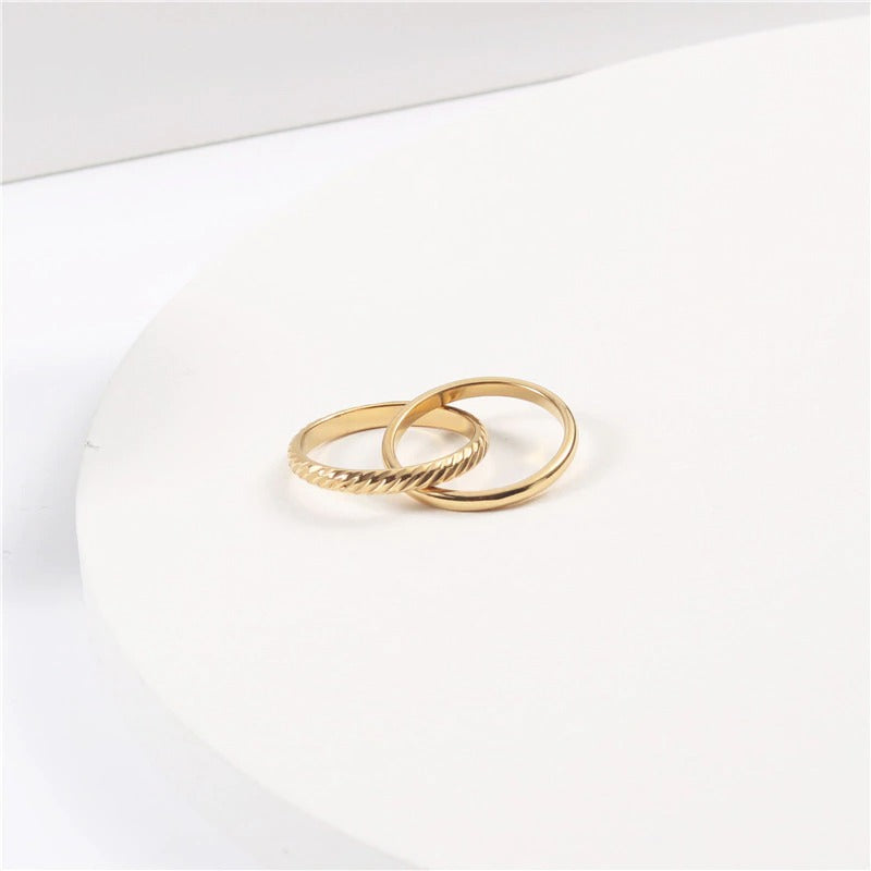 A patterned interlinked gold ring resting on a smooth white surface.