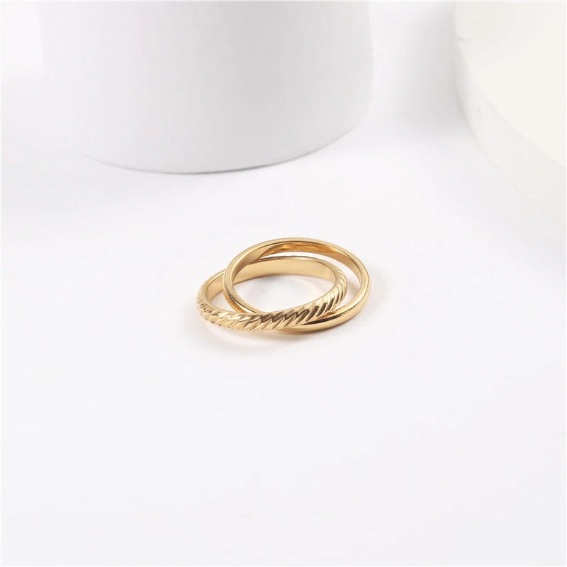 A shiny interlinked gold ring resting on a smooth white surface.