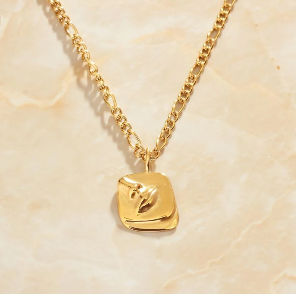 Gold Femme Face Pendant Necklace laid on a marbled background in warm light.