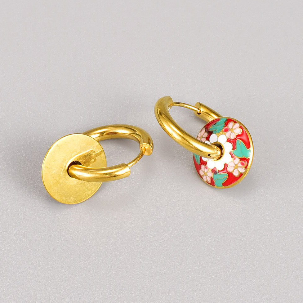 Gold Floral Enamel Loop Earrings laying on a grey surface showing the front and back sides of the gold earrings and floral design.