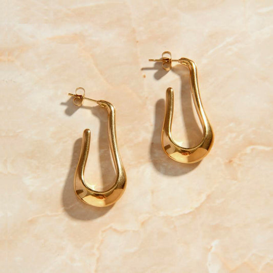 Gold Drop Earrings with a Fluid U-Shaped design laying on a rose quartz surface.