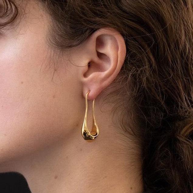 Gold Drop Earrings with a Fluid U-Shaped design being worn by a woman with dark hair.