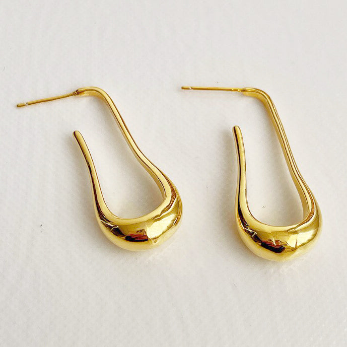 Gold Drop Earrings with a Fluid U-Shaped design laying on a white fabric surface.