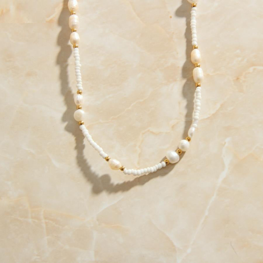 A Gold Freshwater Pearl Chain Bead Necklace laid over a peach coloured marble background.