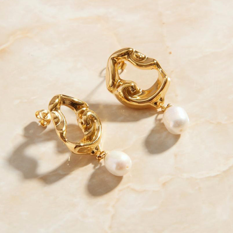 Gold Drop Earrings with Freshwater Pearls laying on a rose quartz surface.