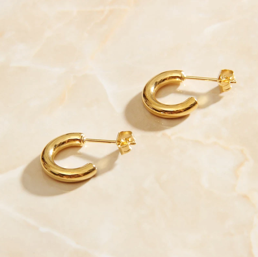 Gold Geo C Earrings laying on a rose quartz surface in warm sunlight.