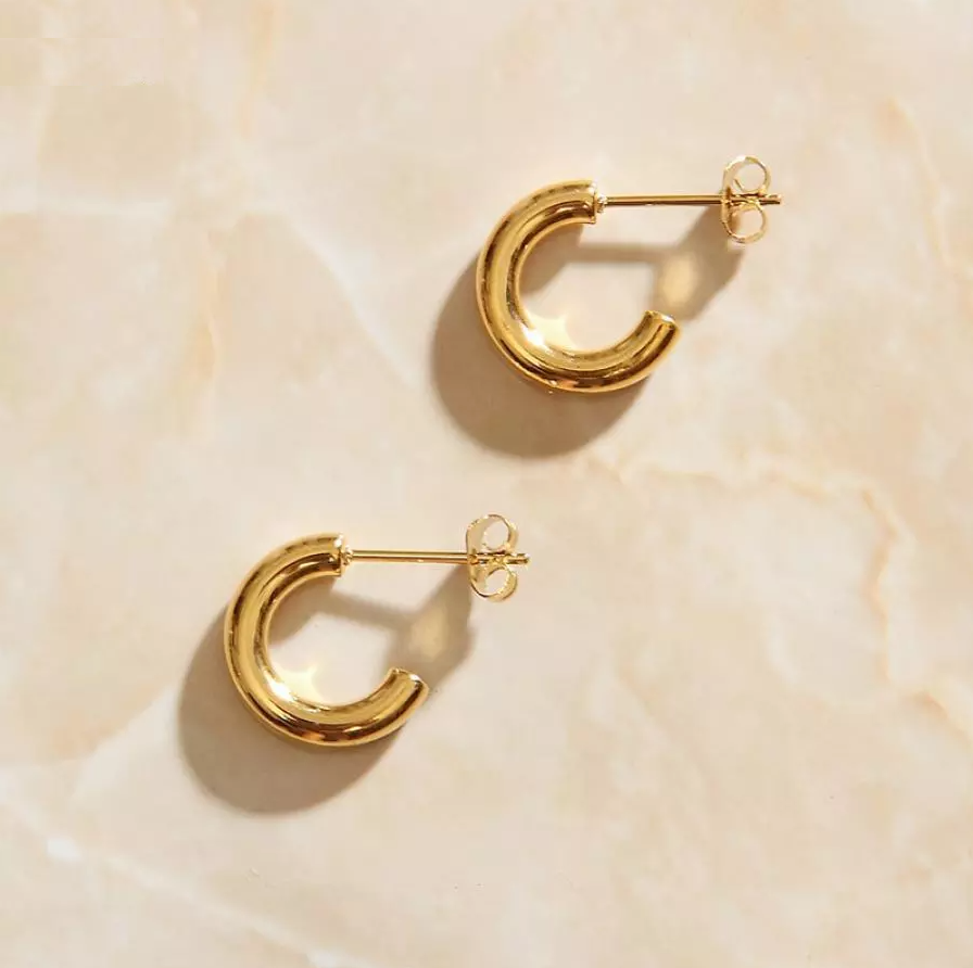 Gold Geo C Earrings laying on a rose quartz surface.