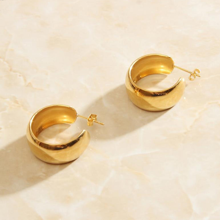 Gold Wide Curved Earrings laying on a smooth rose quartz surface shining brightly.