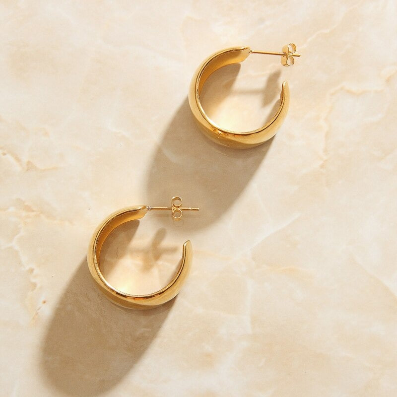 Overhead photograph of Gold Wide Curved Earrings laying on a rose quartz surface.