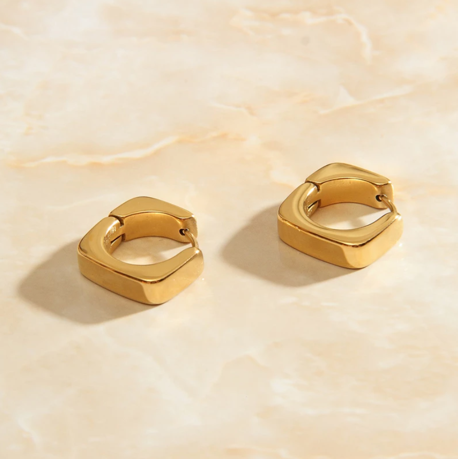 Gold Geo Square Earrings laying on a rose quartz surface.