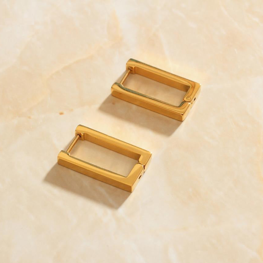 Gold Geometric Rectangle Earrings laying on a rose quartz surface.