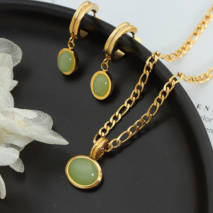 A beautiful Gold Green Stone Set Pendant Chain with matching set of earrings sitting on a black dish.