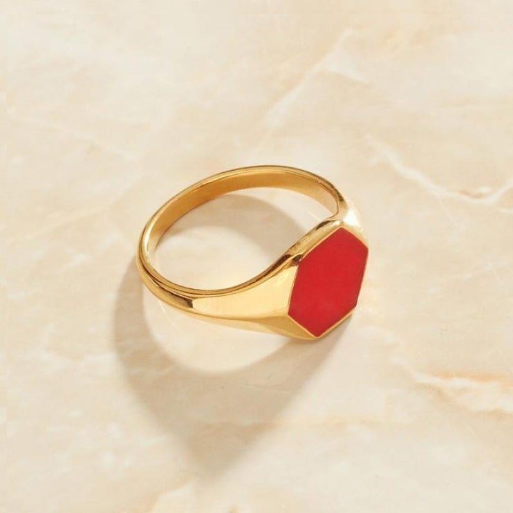 Gold Hexagonal Signet Ring with Red Inlay resting on a smooth marble surface.