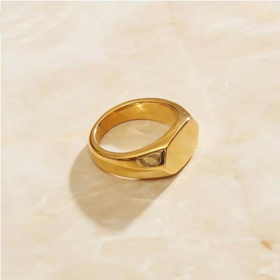 A hexagon gold signet ring resting on a smooth marble surface, showcasing elegance and luxury.