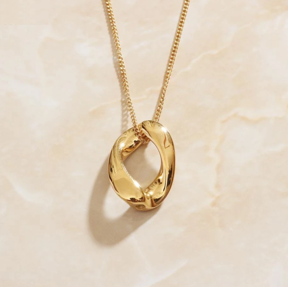 A Gold Infinite Loop Pendant Necklace laying on a marbled background and shining.