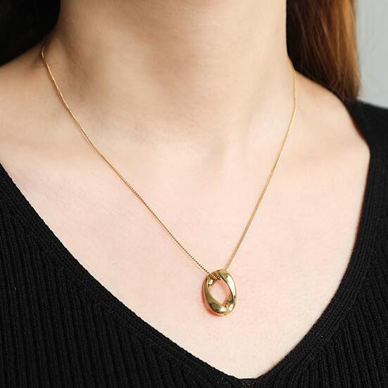 A minimalist Gold Infinite Loop Pendant Necklace worn on a woman's neck with a black top and red hair.