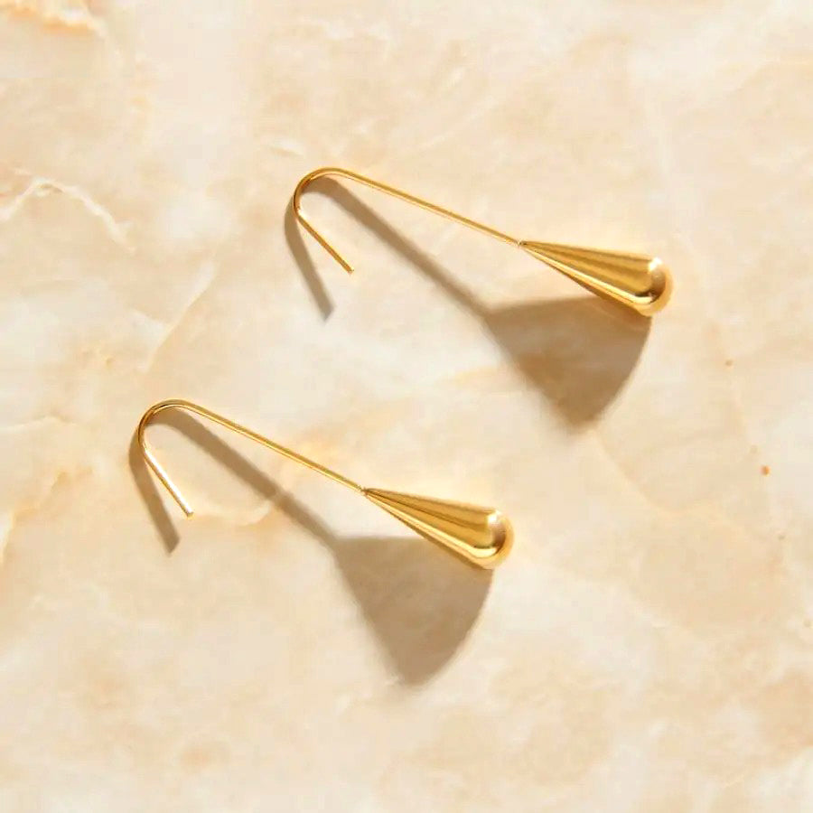 Gold Kudos Tear Drop Earrings laying on a rose quartz surface.