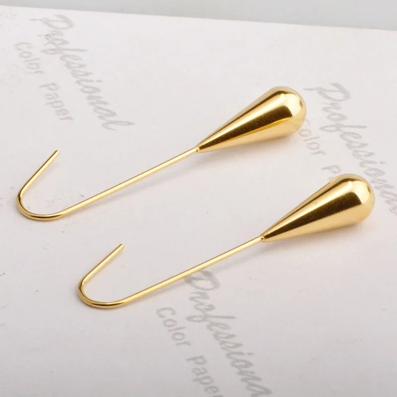 Gold Kudos Tear Drop Earrings laying on a white fabric surface.