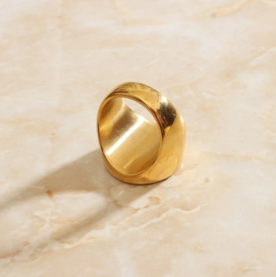 An elegant and luxurious gold signet ring is displayed on a sleek marble surface.