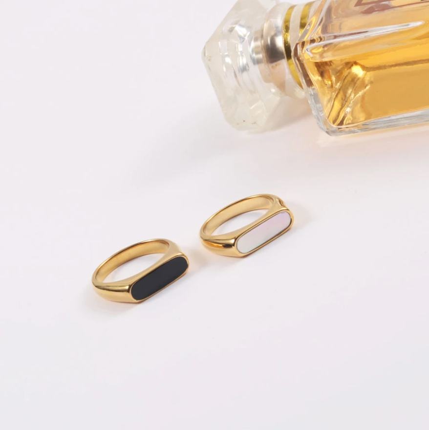 Two Gold Long Black Set Signet Rings on a white surface with a perfume bottle.