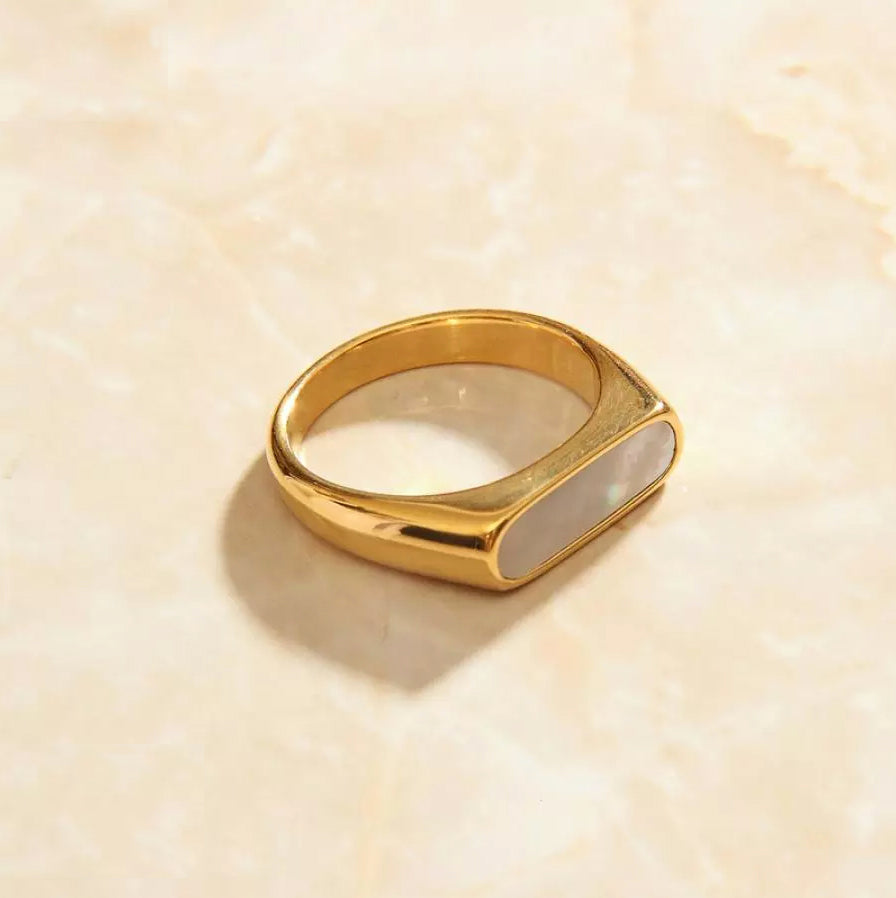 Gold Long Slim Set Signet Ring laying on a smooth marble surface.