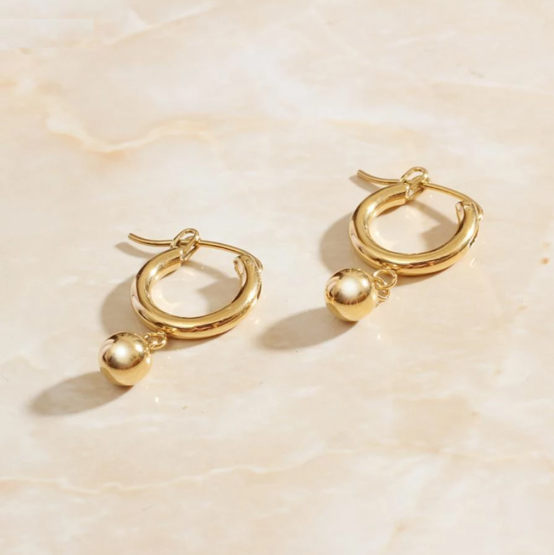 Gold Loop Bead Earrings laying on a rose quartz surface.