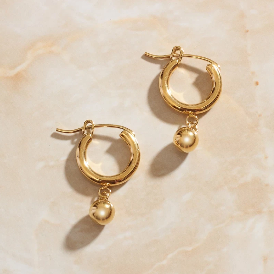 Overhead photograph of Gold Loop Bead Earrings laying on a rose quartz surface.