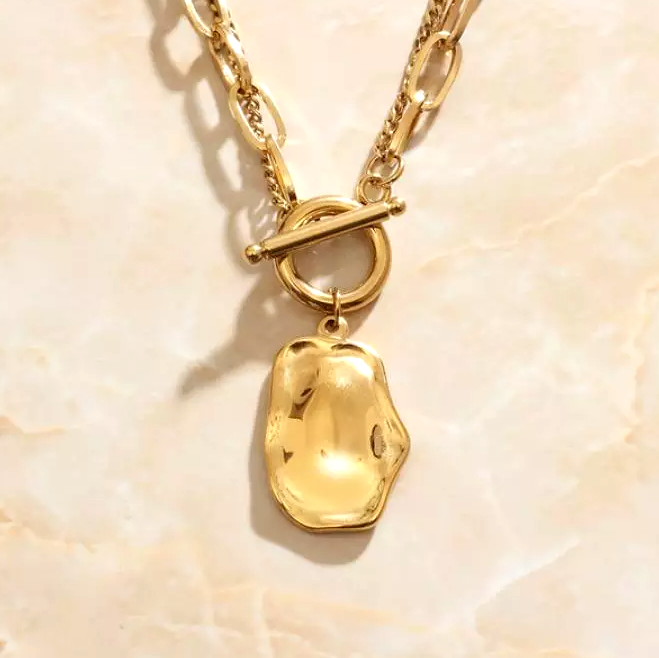Our classic Gold Melt Pendant Necklace shining beautifully on a marbled background.