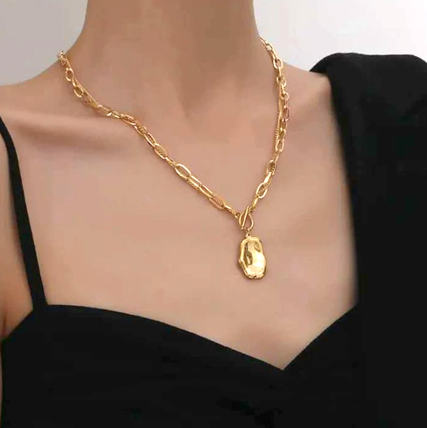 A minimalist Gold Melt Pendant Necklace worn on a woman's neck with a black dress.