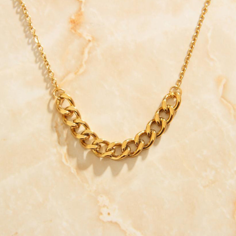 The Gold Mid Chain Necklace laid over a marbled background shining brilliantly.