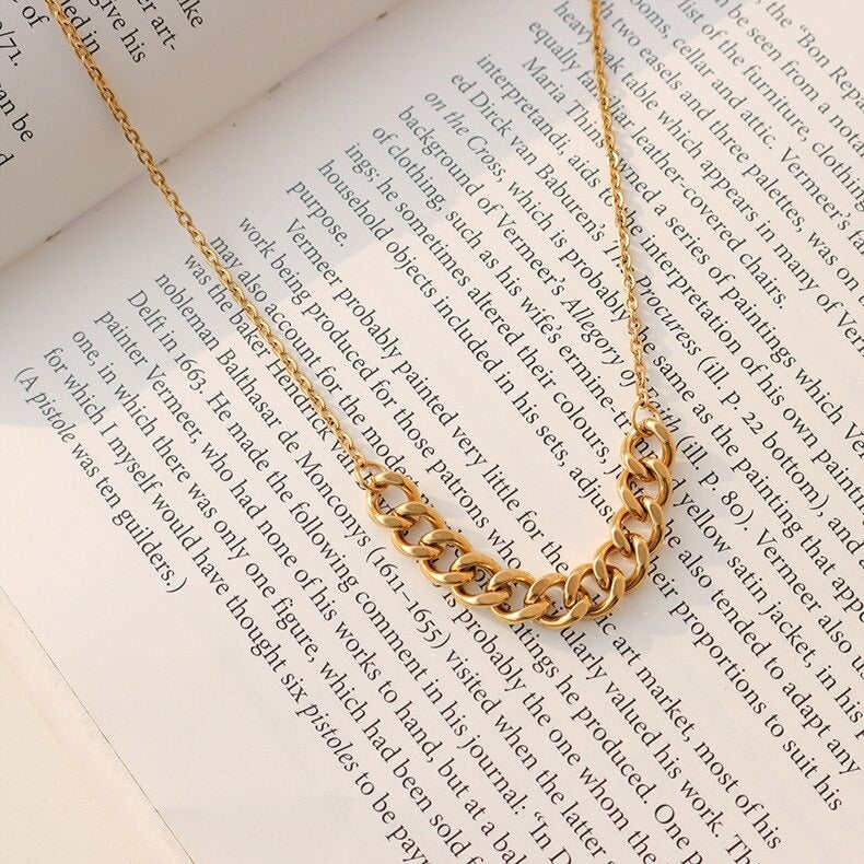 A Gold Mid Chain Necklace draped over a book page.